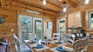 A wooden cabin interior with a dining table set for four, wooden cabinets, and a kitchen area. - Hold My Bear (Pigeon Forge)