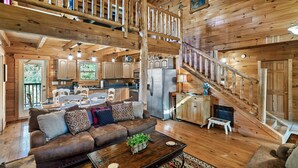 A spacious wooden cabin with a living room, kitchen, and a staircase leading to an upper level. - Hold My Bear (Pigeon Forge)