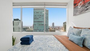 Une chambre avec une grande fenêtre, un lit avec une literie à motifs et une vue sur la ville.