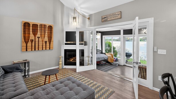 A modern living room with a fireplace, a large window, and a view of the outdoors. - Peaceful Cable Lake Getaway w/ Dock & Views (Dowagiac)