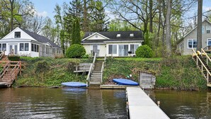 A house with a dock extending into a calm body of water, surrounded by greenery and trees. - Peaceful Cable Lake Getaway w/ Dock & Views (Dowagiac)