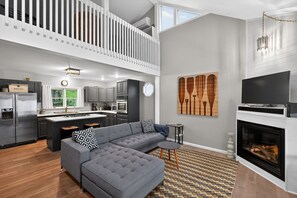 A modern living space with a grey sofa, a fireplace, and a kitchen area. - Peaceful Cable Lake Getaway w/ Dock & Views (Dowagiac)
