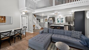A spacious living area with a grey sectional sofa, a dining table with chairs, a kitchen in the background, and a staircase leading to an upper level. - Peaceful Cable Lake Getaway w/ Dock & Views (Dowagiac)