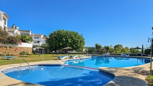 Una piscina con pared de piedra, sillas de descanso y un árbol al fondo.