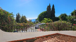 Terraza en la azotea con vistas al mar, rodeada de vegetación exuberante y una barandilla blanca.