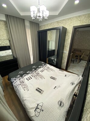 Ein Schlafzimmer mit Bett, Kleiderschrank, Spiegel, einer Kandelaber und Blick auf einen Essbereich.