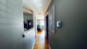 Un couloir avec un plancher en bois, un fauteuil en cuir noir et un réfrigérateur au fond.