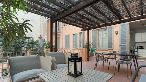Un patio al aire libre con una mesa de madera, sillas, un sofá acolchado y un farol.