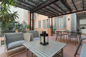 An outdoor patio with a wooden table, chairs, a cushioned sofa, and a lantern. - Brera Apartments in Palestro (Milan)
