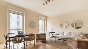Amplia sala de estar con una mesa de comedor, sillas de mimbre, un sofá y dos espejos redondos en las paredes.