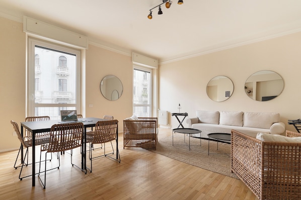 A spacious living area with a dining table, wicker chairs, a sofa, and two round mirrors on the walls. - Brera Apartments in Palestro (Milan)