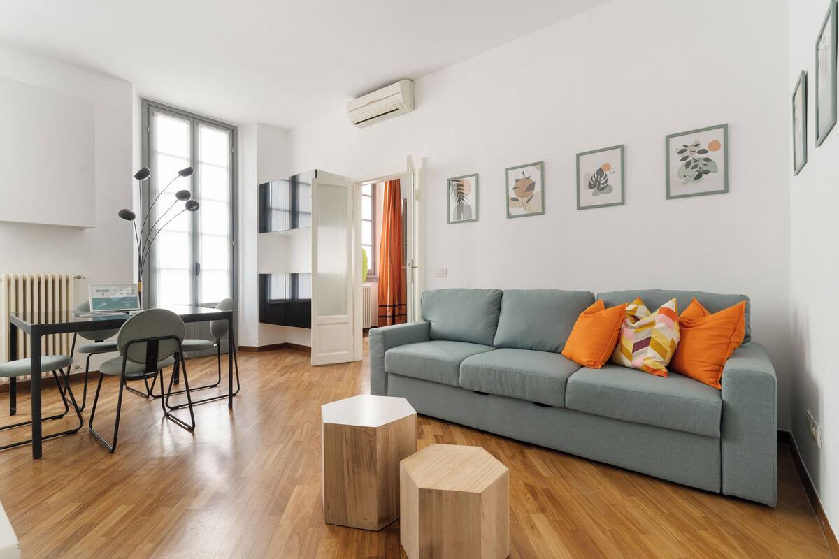 A modern living room with a grey sofa, wooden side tables, and a dining area with a table and chairs.