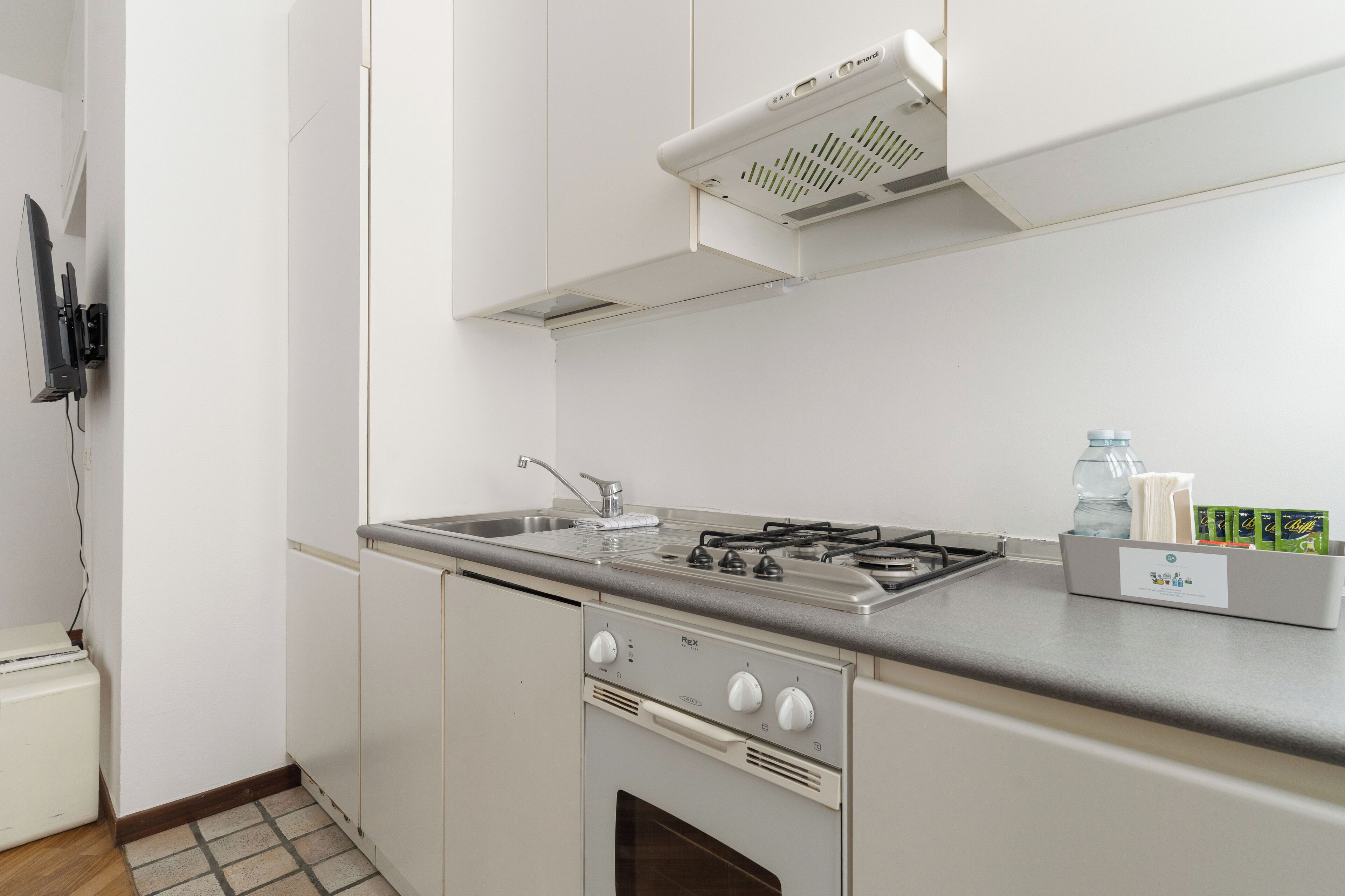 Cocina compacta con estufa a gas, horno y pileta. Se observa un refrigerador pequeño y un microondas a la izquierda.
