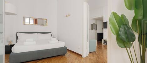 A modern bedroom with a bed, bedside table, lamp, and a large green plant.