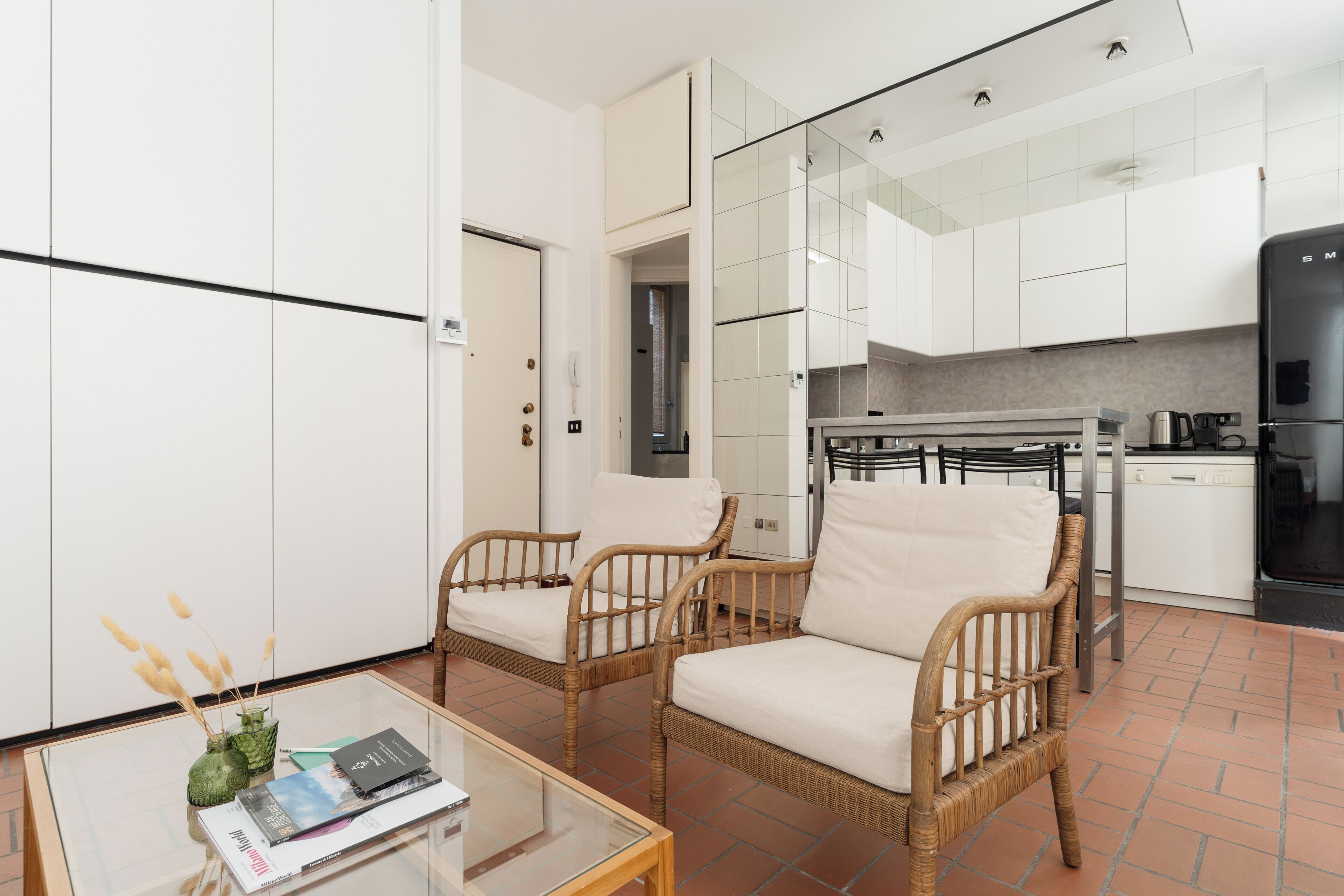 A modern kitchen with white cabinets, a black refrigerator, and a dining area with wicker chairs and a glass table.