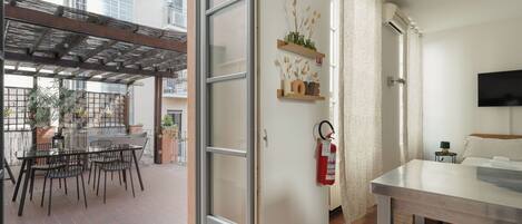 An open door leading to a balcony with a table and chairs, a fire extinguisher on the wall, and a TV mounted on the wall.