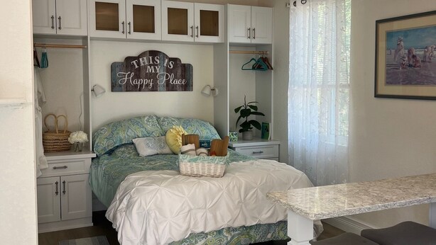 A bedroom with a bed, a desk, a chair, a ceiling fan, and a window with curtains.