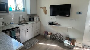 A modern kitchen with white cabinets, a built-in microwave, a large window, and a flat-screen TV mounted on the wall.