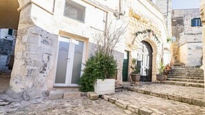 Un patio empedrado con una puerta blanca que dice “White Stones”, un pequeño árbol y una escalera que sube a un nivel superior.