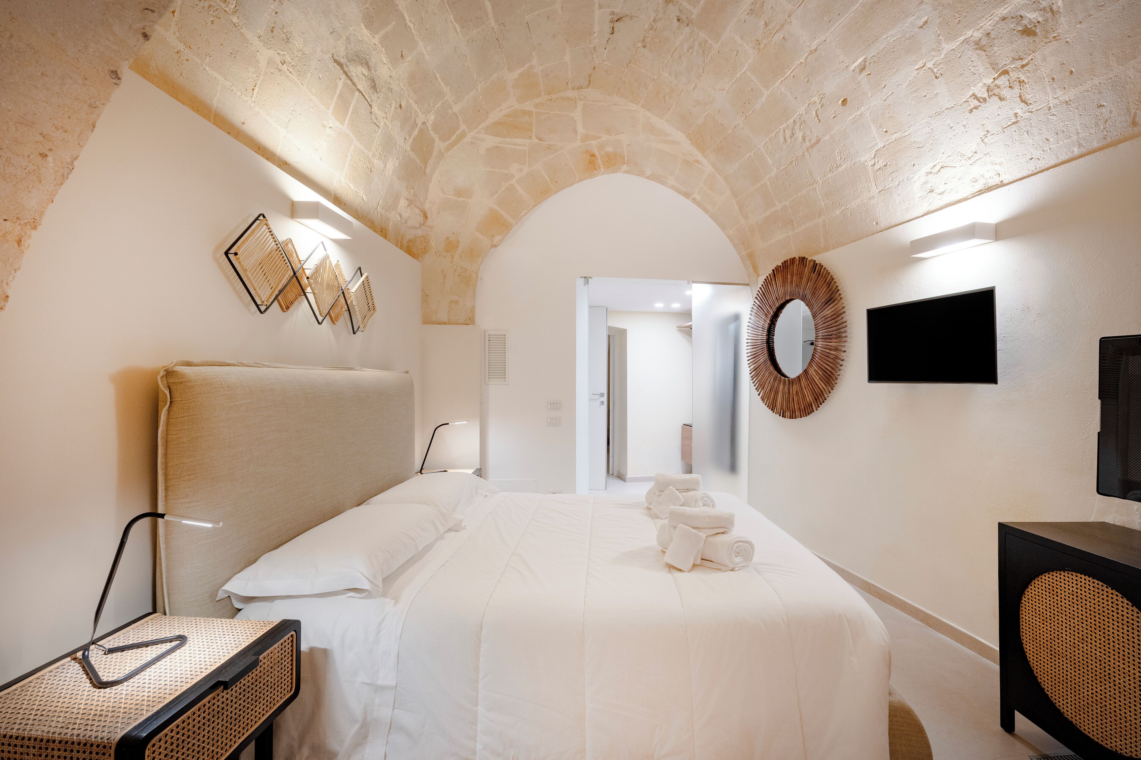 A hotel room with a stone arch ceiling, a bed with white linens, a flat-screen TV, and a woven wall decoration.