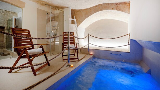 Zona de spa con hidromasaje, sillas de madera y separador de vidrio.
