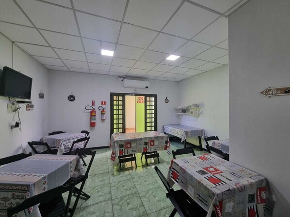 A hotel room with a tiled floor, a television mounted on the wall, a fire extinguisher, a small shelf with cups, and a sign that says "Coffee". - QUARTUS HOTEL (Costa Rica)