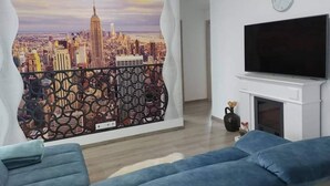 Un salon avec une fresque représentant un paysage urbain, un téléviseur à écran plat et une cheminée.
