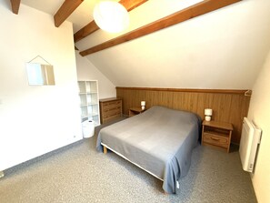 Ein Schlafzimmer mit schrägem Dach, einem Bett mit grauer Bettdecke, zwei Nachttischen mit Lampen, einem hölzernen Kopfteil und einem weißen Kleiderschrank.