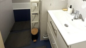 Kylpyhuone, jossa on valkoinen pesuallas, peili ja pieni puinen jakkara.