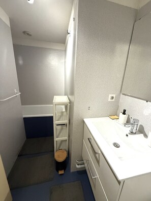 Ein Badezimmer mit einem weißen Waschbecken, einem Spiegel und einem kleinen hölzernen Hocker.