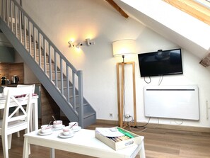 A modern living space with a staircase, a dining area with white furniture, a flat-screen TV mounted on the wall, and a floor lamp. - 2 bedrooms with a mezzanine and south-facing doors (Le Lioran)
