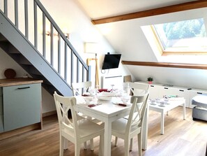 Ein Essbereich mit einem weißen Tisch und Stühlen, einer Treppe und einem an der Wand befestigten Fernseher.