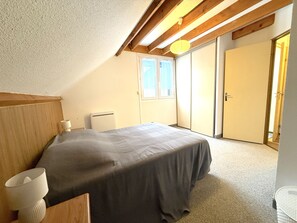 Ein Schlafzimmer mit Bett, Nachttisch, Lampe, Heizkörper, Kleiderschrank und einer Tür.