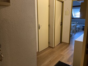 Ein Flur mit Holzboden, einer geschlossenen Tür und Blick in einen Essbereich mit Tisch und Stühlen.