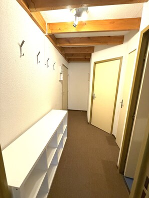 Ein schmaler Flur mit Holzboden und einer weißen Wand mit Haken.