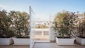 An open glass door leading to a terrace with potted plants and a view of buildings in the background. - 2BR Apartment in Bari, Casa Costa Sud | Private Garden + BBQ + Full Kitchen (Bari)
