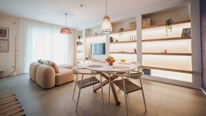 A modern living room with a round dining table, beige sofas, and a TV mounted on the wall. - 2BR Apartment in Bari, Casa Costa Sud | Private Garden + BBQ + Full Kitchen (Bari)