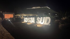 Illuminated 'COSTA SUD' sign in front of a building with a modern design. - 2BR Apartment in Bari, Casa Costa Sud | Private Garden + BBQ + Full Kitchen (Bari)