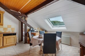 Zona de menjador amb taula i cadires, cuina amb armaris de fusta i un fanal.