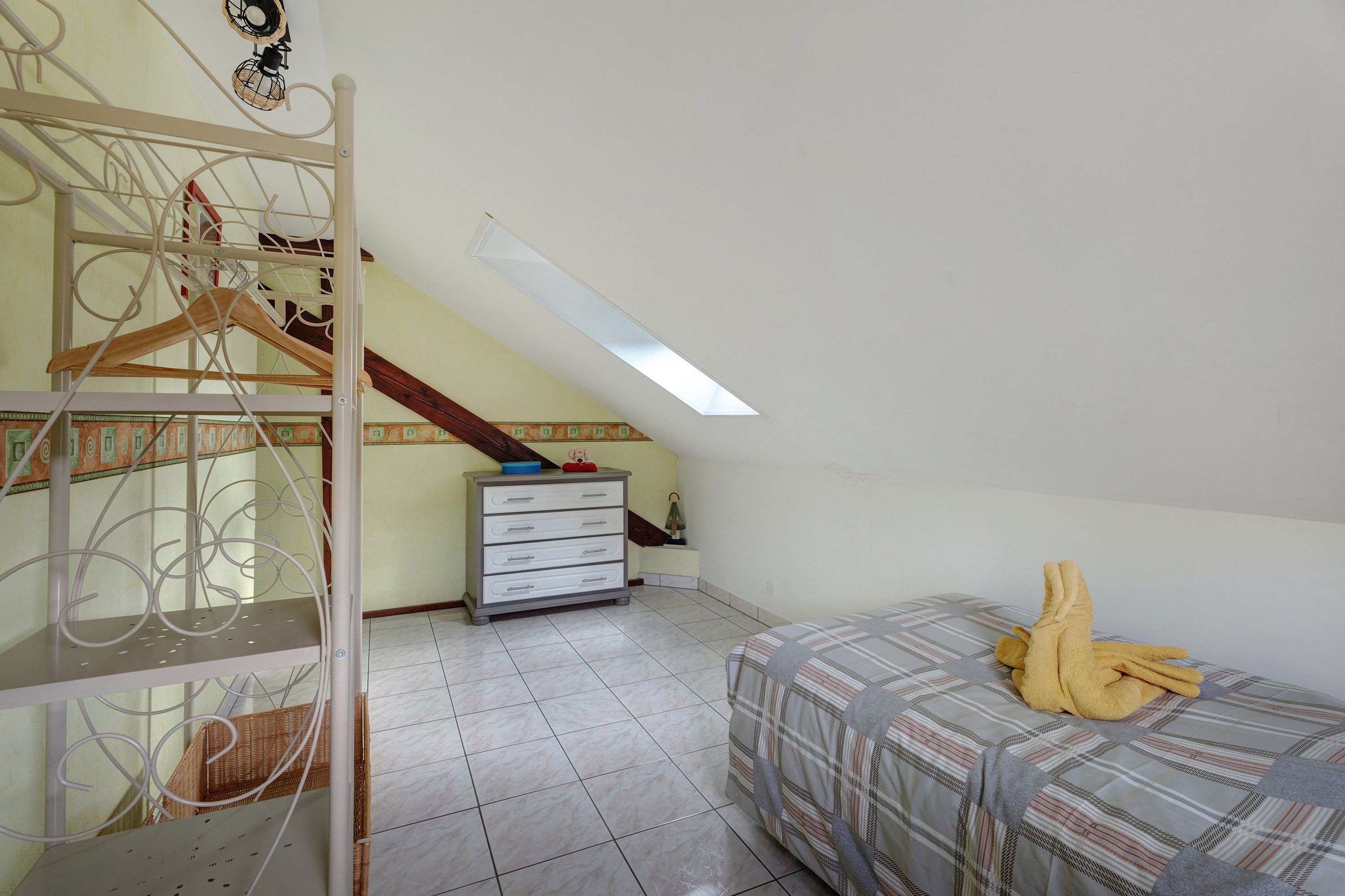 A bedroom with a sloped ceiling, a bed with a plaid duvet, a dresser, and a metal wardrobe with a hanging rack.