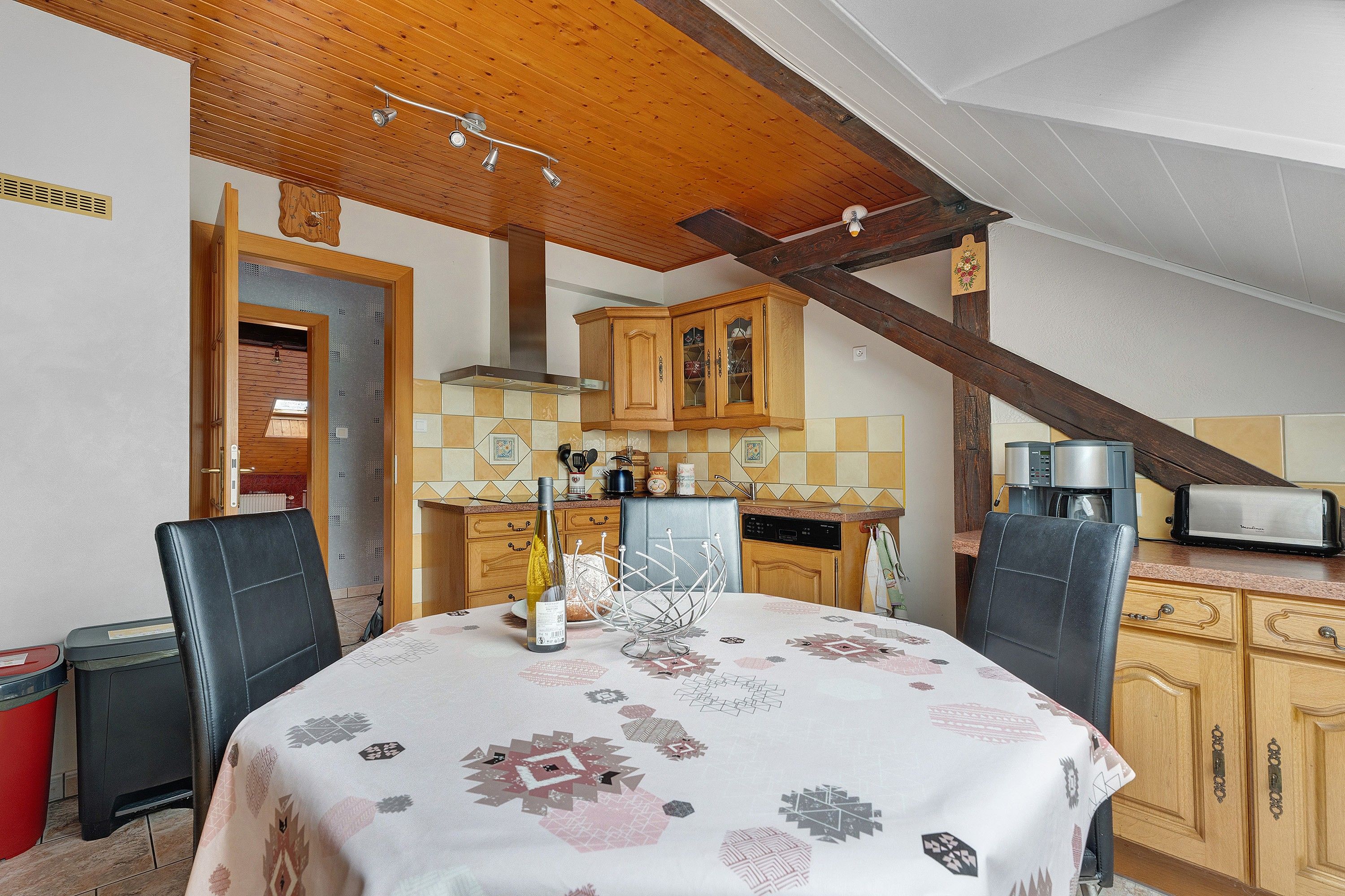 Un comedor con una mesa dispuesta para dos, una cocina al fondo y un techo de madera.