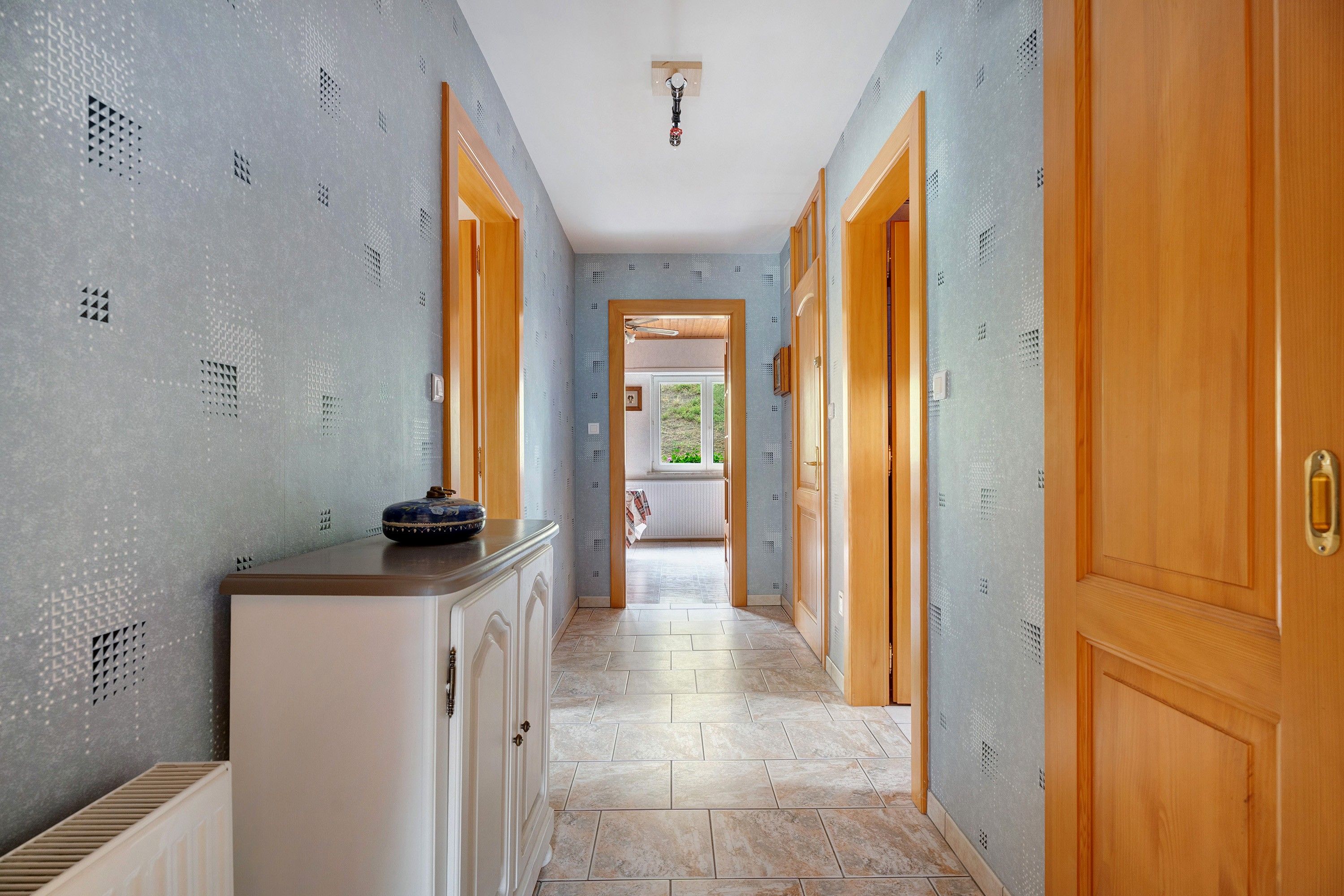 A hallway with patterned walls, wooden doors, and a tiled floor.