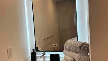 A modern bathroom with a large mirror, white countertop, and a stack of towels.
