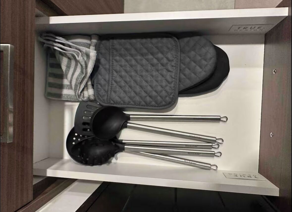 Un tiroir de cuisine contenant une spatule noire, une casserole noire et une poêle noire.