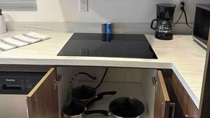 Een compacte keuken met een inbouwfornuis, een magnetron en een koffiezetapparaat. Er zijn kastjes boven en onder het aanrecht, en een vaatwasser is gedeeltelijk links zichtbaar.