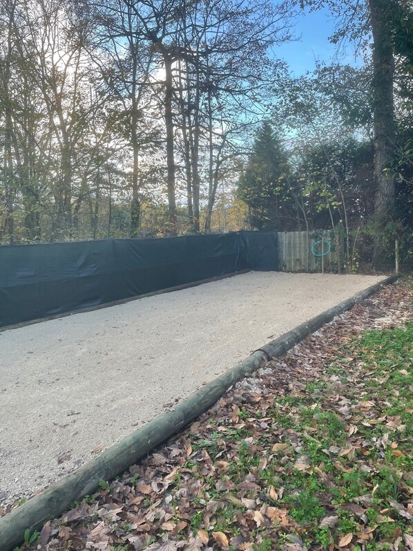 Una cancha de grava con borde verde, rodeada de árboles y una valla de madera.