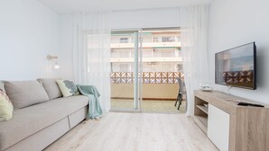 Een moderne woonkamer met een bank, een televisie en een schuifdeur naar een balkon.