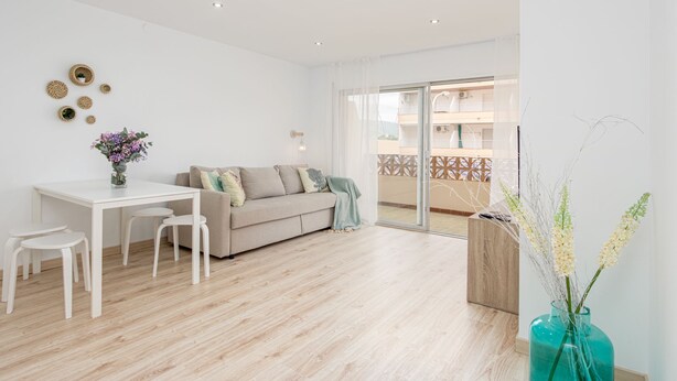 Een moderne woonkamer met een bank, een eettafel met stoelen en een groot raam met uitzicht op een balkon.