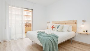 Een slaapkamer met een houten hoofdbord, een bed met witte beddengoed, een groen geborduurd plaid, een zeester decoratie en een klein plankje met planten.