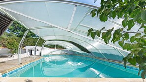 Une piscine dotée d’une structure en verre, entourée d’un jardin et d’un bâtiment.